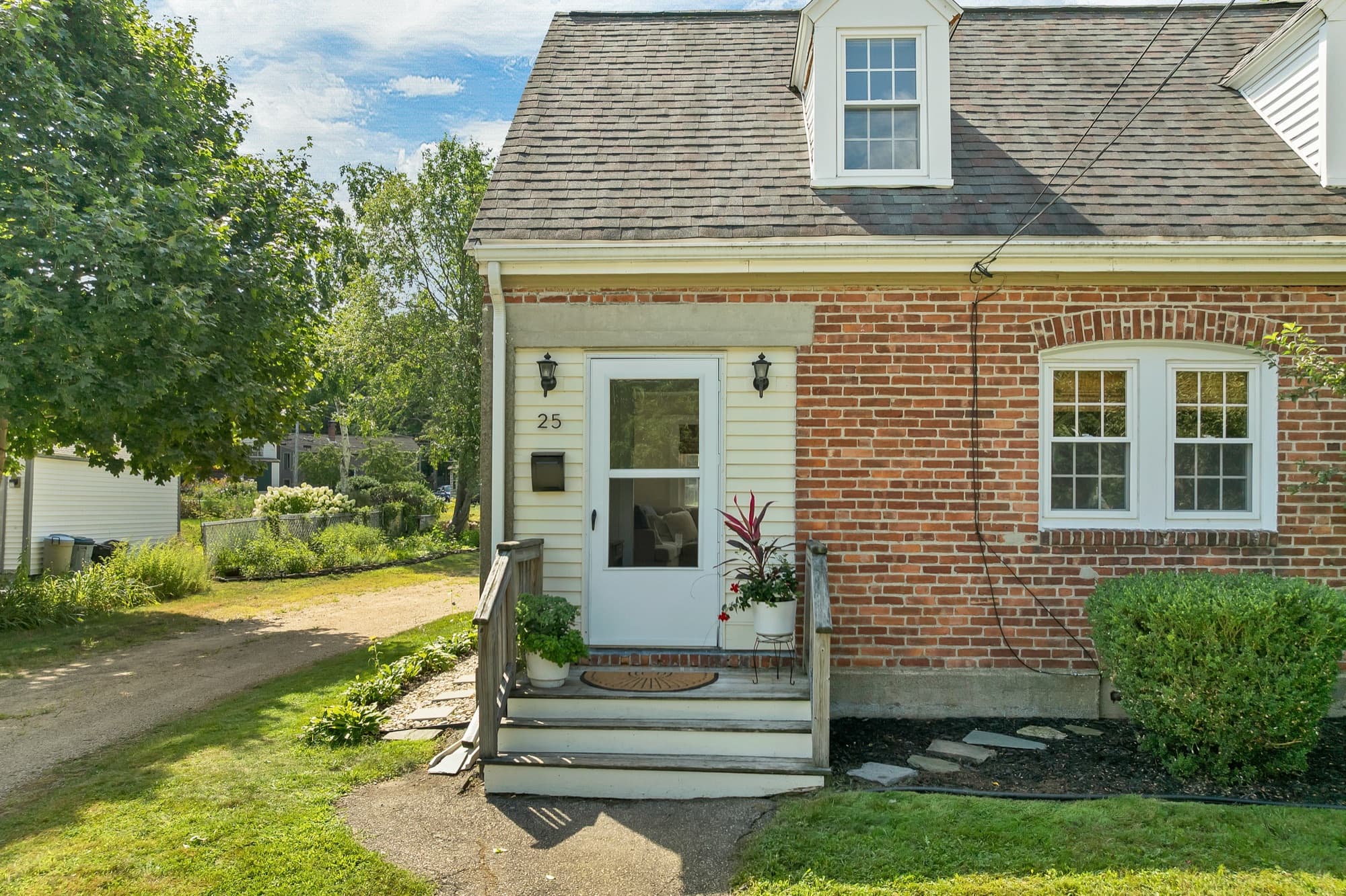 Unit 25's entrance, with a storm door, brick front, and plantings