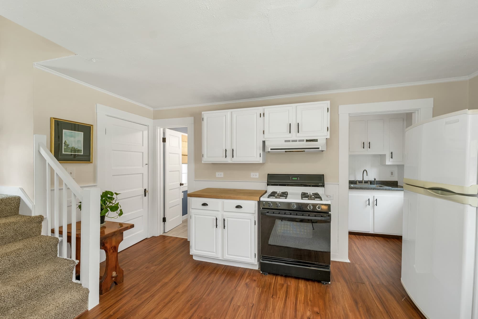 Unit 25 kitchen with white cabinets, gas range, and the carpeted stairs beyond