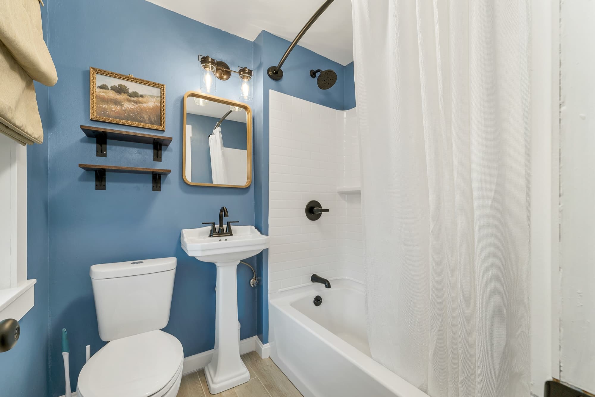 Unit 25's remodeled bath: pedestal sink, tub with shower, tile floor, and blue walls